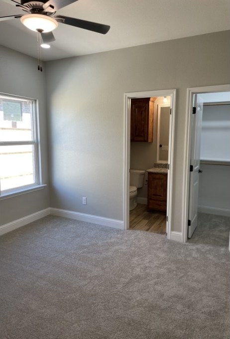 unfurnished bedroom featuring a walk in closet, connected bathroom, baseboards, and light carpet