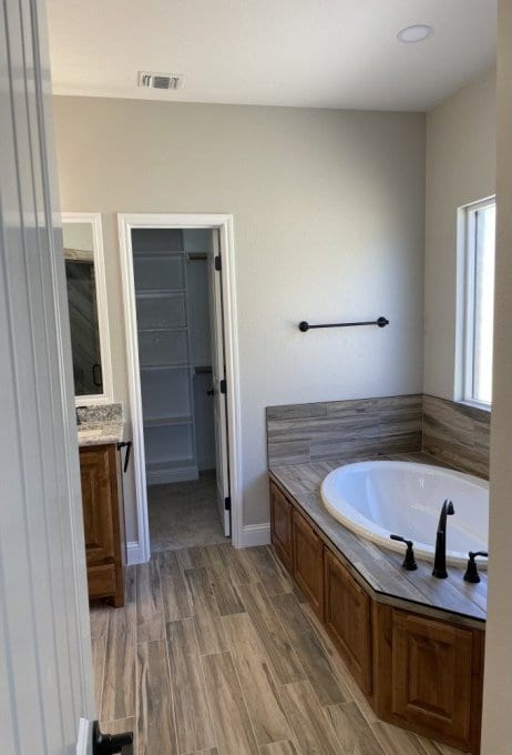 full bathroom with a walk in closet, baseboards, a garden tub, wood finished floors, and vanity