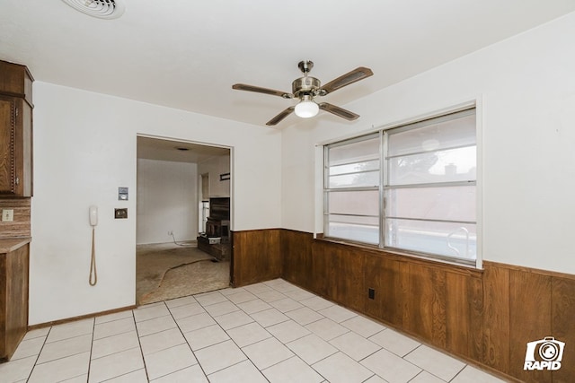 unfurnished room featuring a wood stove, wooden walls, and ceiling fan