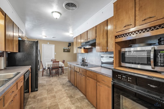 kitchen with baseboards, visible vents, brown cabinetry, under cabinet range hood, and black appliances