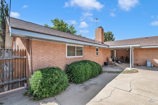 back of house featuring a patio, brick siding, fence, roof with shingles, and a chimney