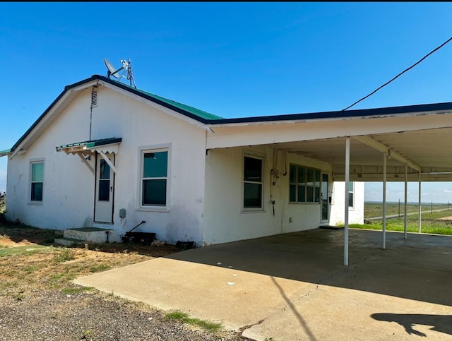 rear view of house with an attached carport, concrete driveway, and stucco siding