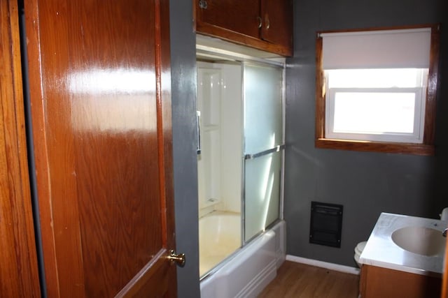 full bath featuring bath / shower combo with glass door, wood finished floors, vanity, baseboards, and heating unit