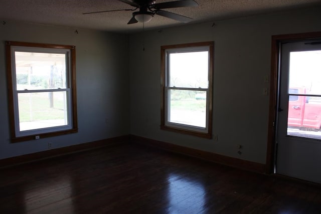 empty room featuring a textured ceiling, dark wood finished floors, and baseboards