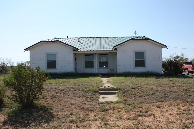 rear view of house featuring stucco siding, metal roof, and a yard