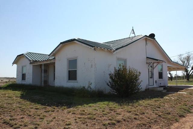 view of side of property with a lawn, an attached carport, metal roof, a standing seam roof, and stucco siding