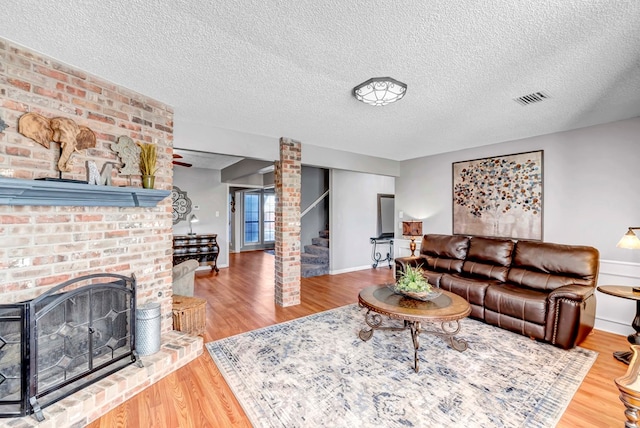 living room with hardwood / wood-style floors, a textured ceiling, and a brick fireplace