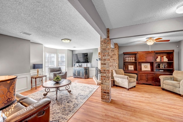 living room with a textured ceiling, light hardwood / wood-style flooring, ceiling fan, and ornate columns