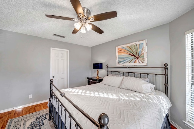 bedroom with ceiling fan, wood-type flooring, and a textured ceiling