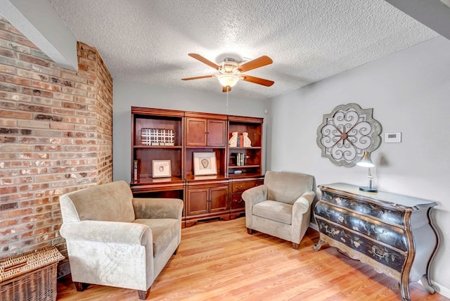 living area with ceiling fan, light hardwood / wood-style floors, and a textured ceiling