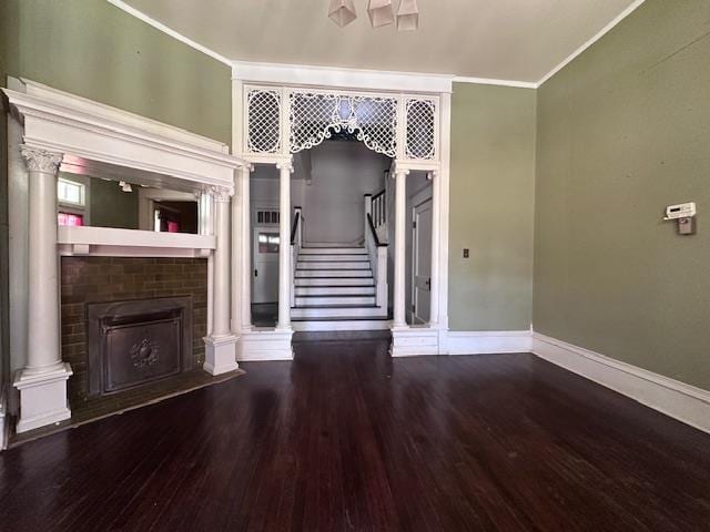 2311 30th St, Snyder, TX 79549 - unfurnished living room featuring wood finished floors, a brick fireplace, stairs, ornamental molding, and decorative columns