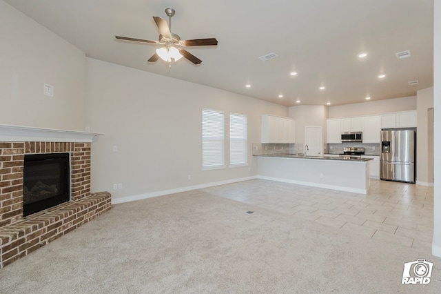 unfurnished living room featuring light tile patterned floors, sink, a brick fireplace, and ceiling fan