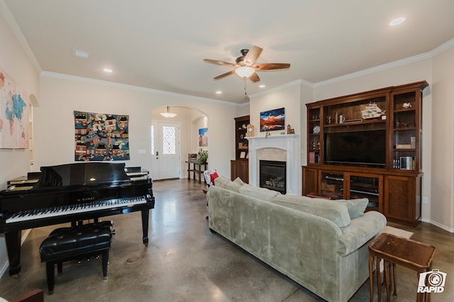 living area featuring arched walkways, a ceiling fan, finished concrete floors, ornamental molding, and a glass covered fireplace