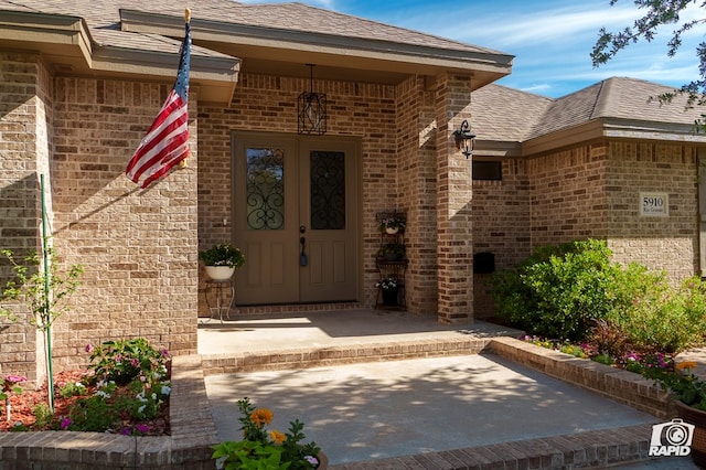 property entrance featuring brick siding and a shingled roof