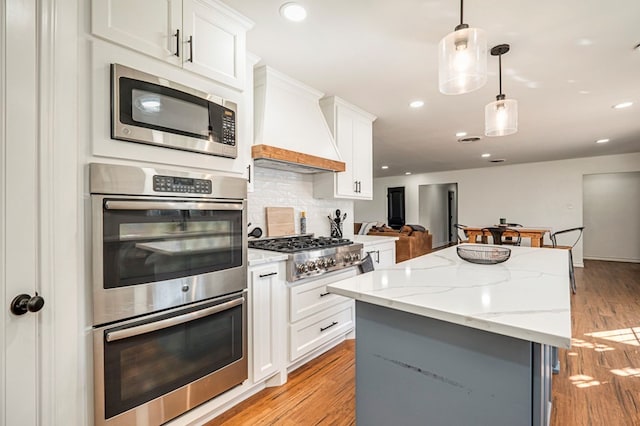 kitchen with premium range hood, white cabinetry, appliances with stainless steel finishes, tasteful backsplash, and decorative light fixtures