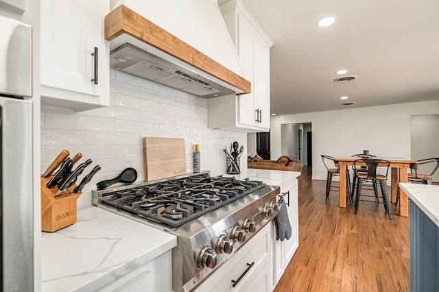 kitchen featuring appliances with stainless steel finishes, white cabinetry, decorative backsplash, light stone counters, and custom range hood