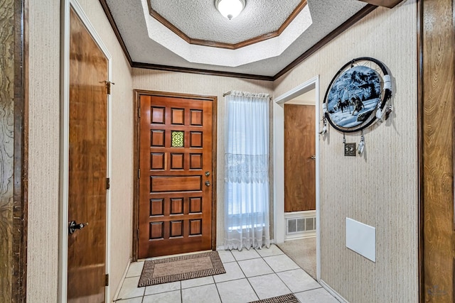 entrance foyer with a textured ceiling, light tile patterned flooring, visible vents, ornamental molding, and a tray ceiling