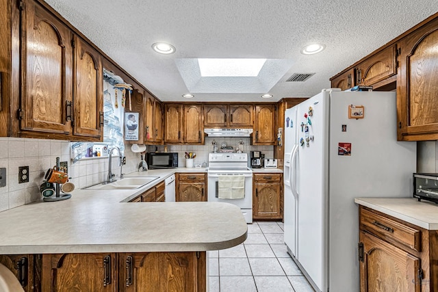 kitchen featuring a peninsula, white appliances, light countertops, and under cabinet range hood