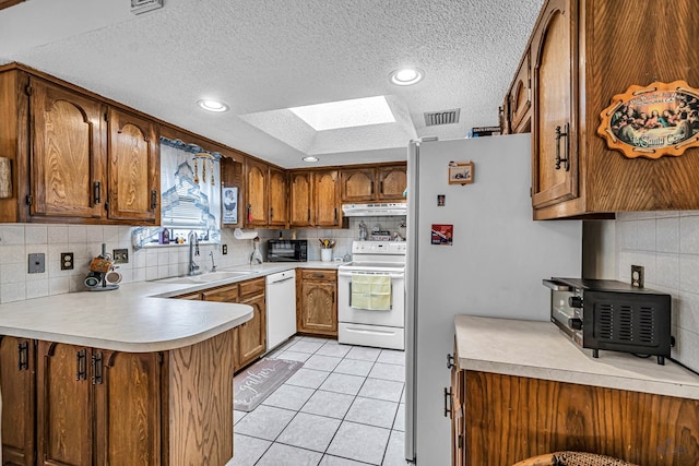 kitchen featuring white appliances, a skylight, a sink, light countertops, and brown cabinets