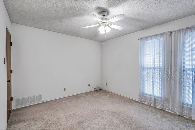 unfurnished room featuring light carpet, a textured ceiling, visible vents, and a ceiling fan