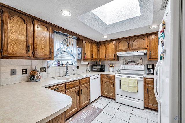 kitchen featuring light countertops, white appliances, under cabinet range hood, and brown cabinets