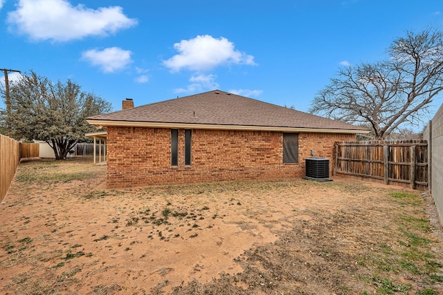 rear view of house featuring a fenced backyard, a chimney, roof with shingles, cooling unit, and brick siding