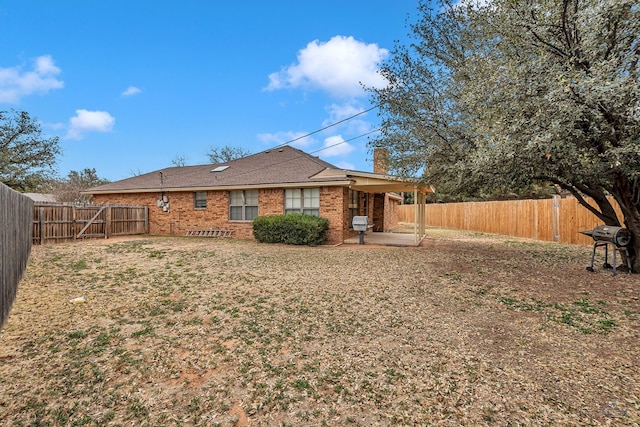 back of house featuring a fenced backyard, a patio, a chimney, and brick siding