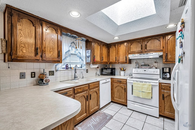 kitchen featuring white appliances, brown cabinetry, light countertops, under cabinet range hood, and a sink