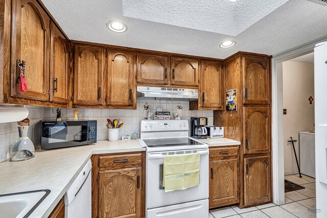 kitchen featuring white appliances, tasteful backsplash, brown cabinets, light countertops, and under cabinet range hood