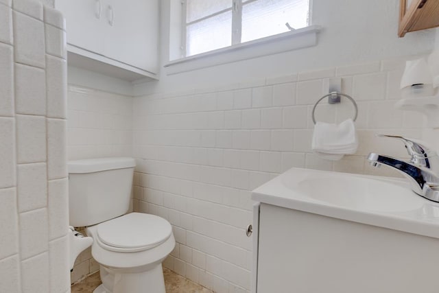 bathroom with toilet, a wainscoted wall, vanity, and tile walls