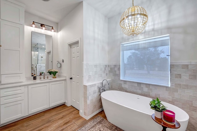 bathroom featuring a chandelier, tile walls, vanity, hardwood / wood-style floors, and a washtub