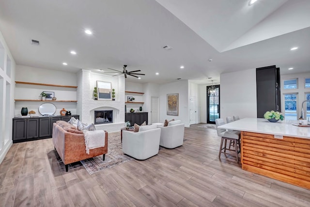 living room featuring a large fireplace, ceiling fan, and light hardwood / wood-style flooring