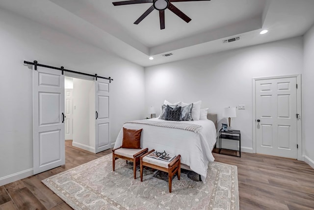 bedroom featuring hardwood / wood-style flooring, a barn door, and a raised ceiling