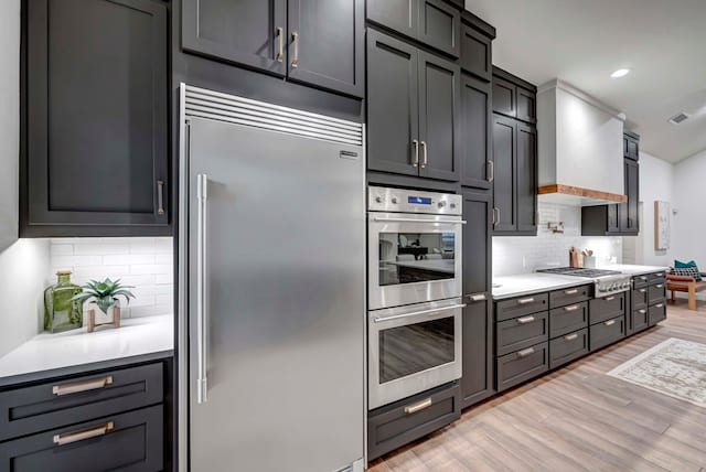 kitchen featuring premium range hood, stainless steel appliances, light hardwood / wood-style floors, and tasteful backsplash