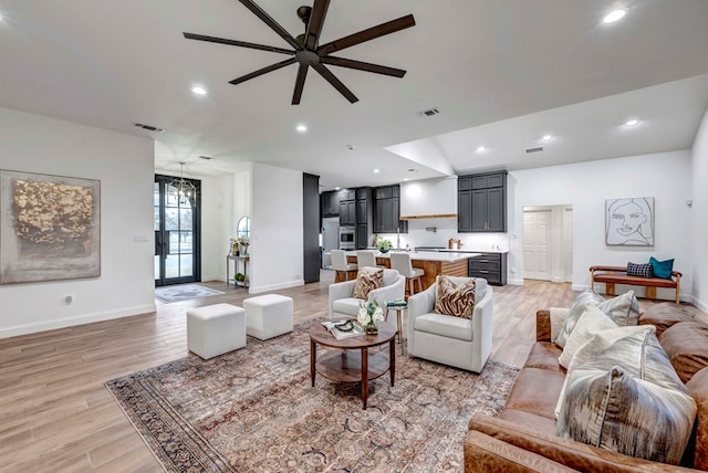 living room with ceiling fan with notable chandelier and light hardwood / wood-style flooring