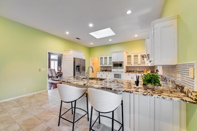 kitchen with kitchen peninsula, a skylight, stainless steel appliances, sink, and white cabinets