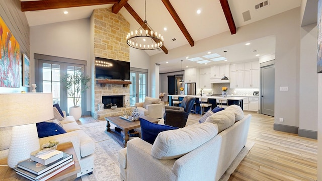 living room featuring high vaulted ceiling, a stone fireplace, beamed ceiling, light wood-style floors, and a chandelier
