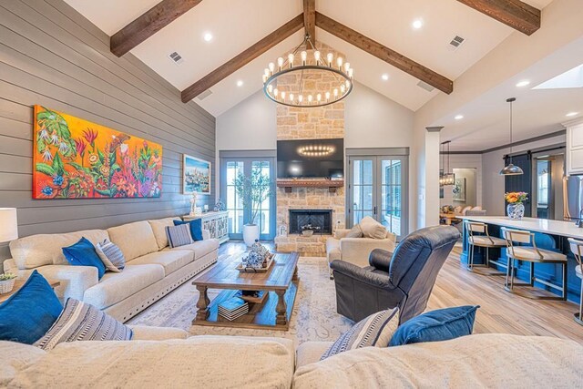 living room featuring high vaulted ceiling, light wood-style floors, beam ceiling, a chandelier, and wood walls
