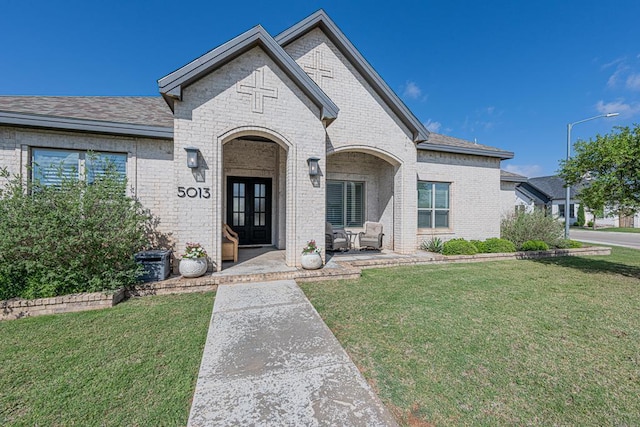 french provincial home featuring brick siding, french doors, and a front yard