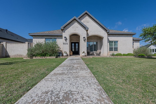 french country inspired facade featuring brick siding, a front yard, and french doors