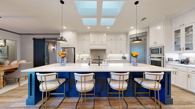 kitchen featuring stainless steel appliances, light wood-type flooring, tasteful backsplash, white cabinetry, and a large island with sink