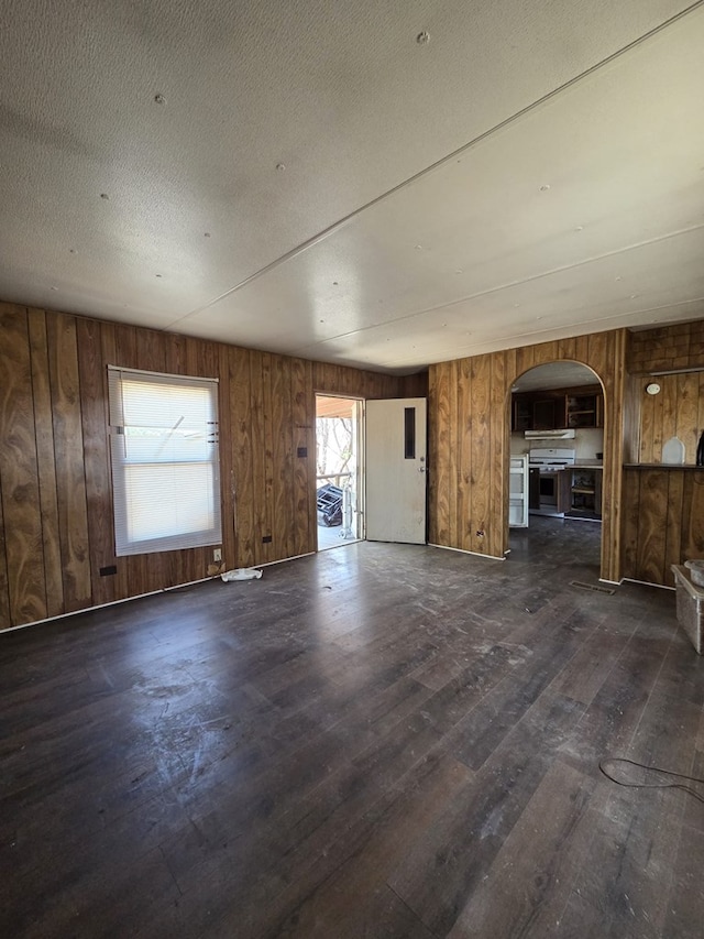 6208 E County Rd 84, Midland, TX 79706 - unfurnished living room featuring arched walkways, dark wood-style flooring, and wood walls