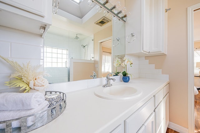 bathroom featuring tiled shower, vanity, visible vents, and baseboards