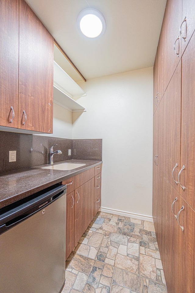 kitchen with tasteful backsplash, stone finish floor, a sink, dishwasher, and baseboards