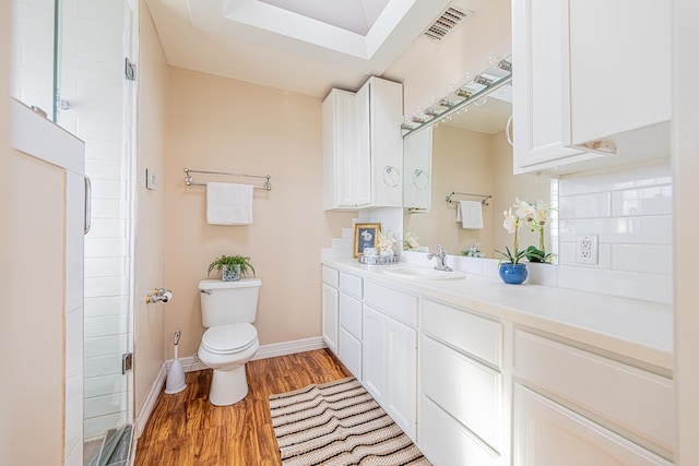 bathroom with toilet, wood finished floors, vanity, visible vents, and decorative backsplash