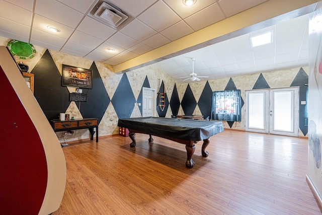 rec room with a paneled ceiling, visible vents, wood finished floors, baseboards, and wallpapered walls