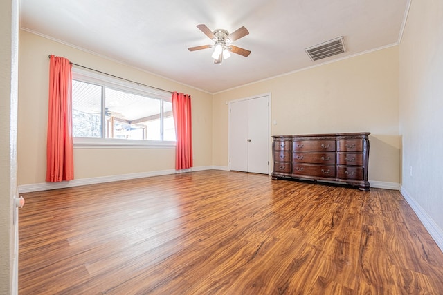 empty room with ceiling fan, wood finished floors, visible vents, baseboards, and ornamental molding