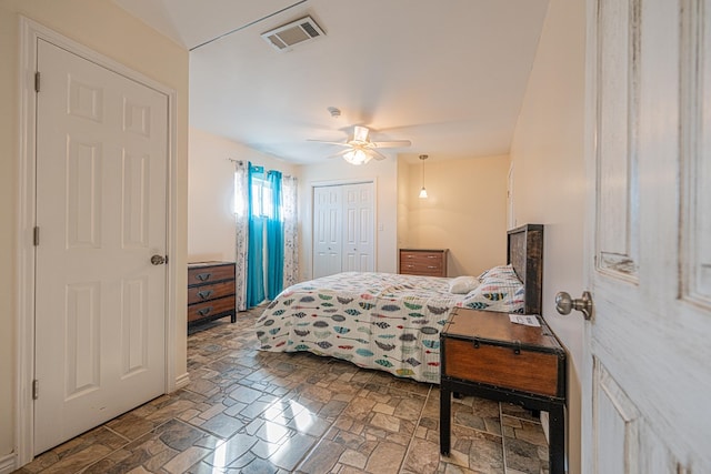 bedroom featuring a ceiling fan, stone finish flooring, visible vents, and a closet