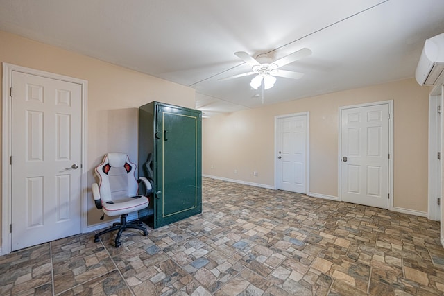 interior space featuring stone finish floor, a wall unit AC, ceiling fan, and baseboards