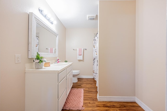 full bath with baseboards, vanity, toilet, and wood finished floors